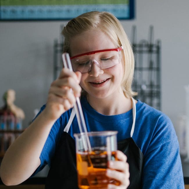 A student happily working on a science experiment, stirring liquid in a beaker.