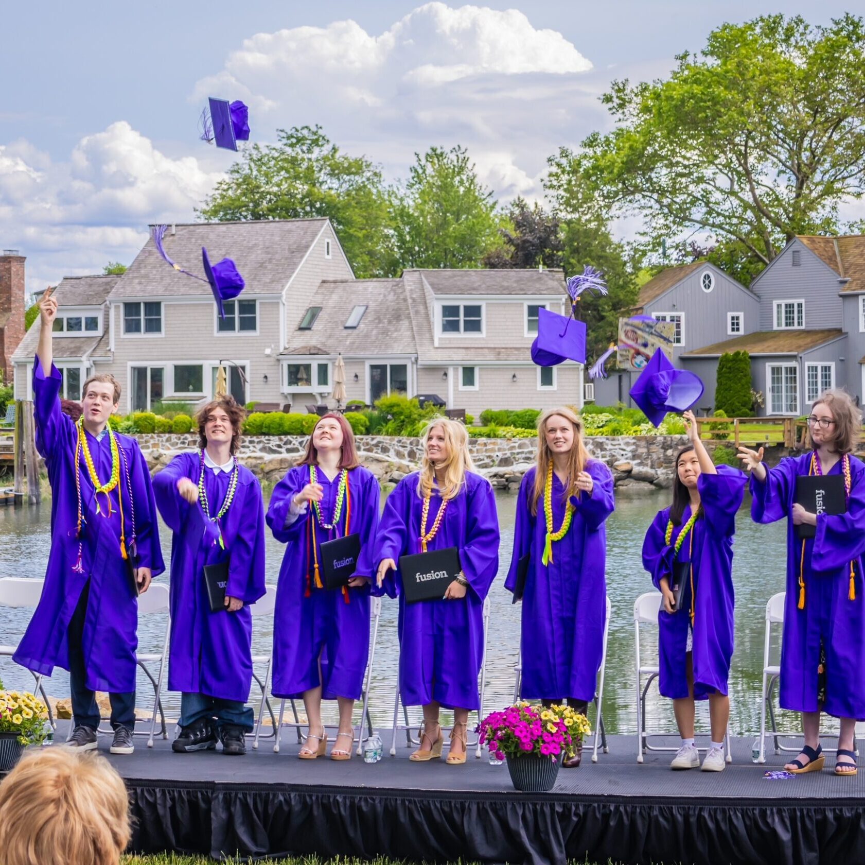 Fusion grads are gathered on stage in their caps and gowns, some throwing their hats into the air.